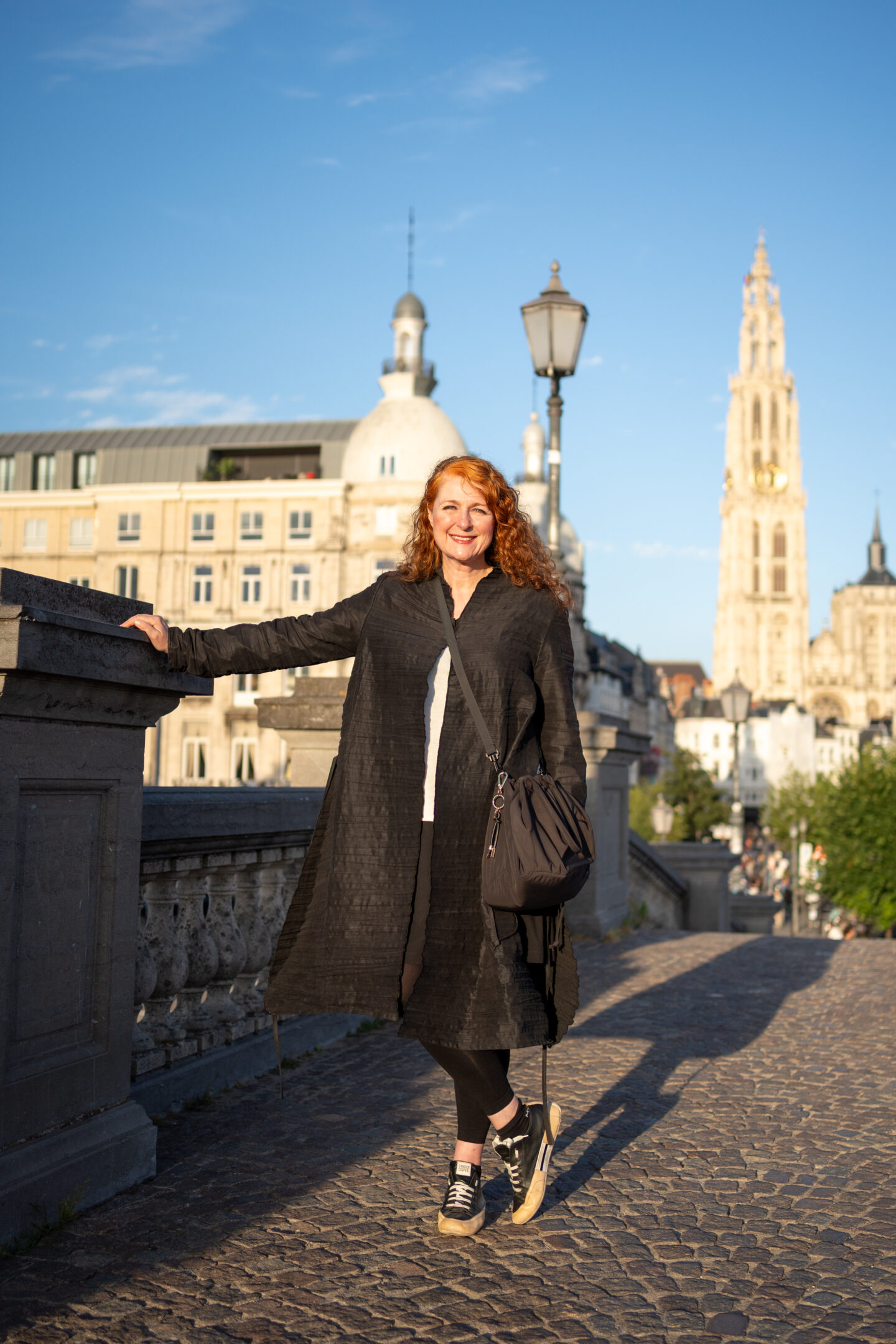 Woman wearing a black UNIQLO travel bag in Antwerp with the Cathedral of Our Lady in the background