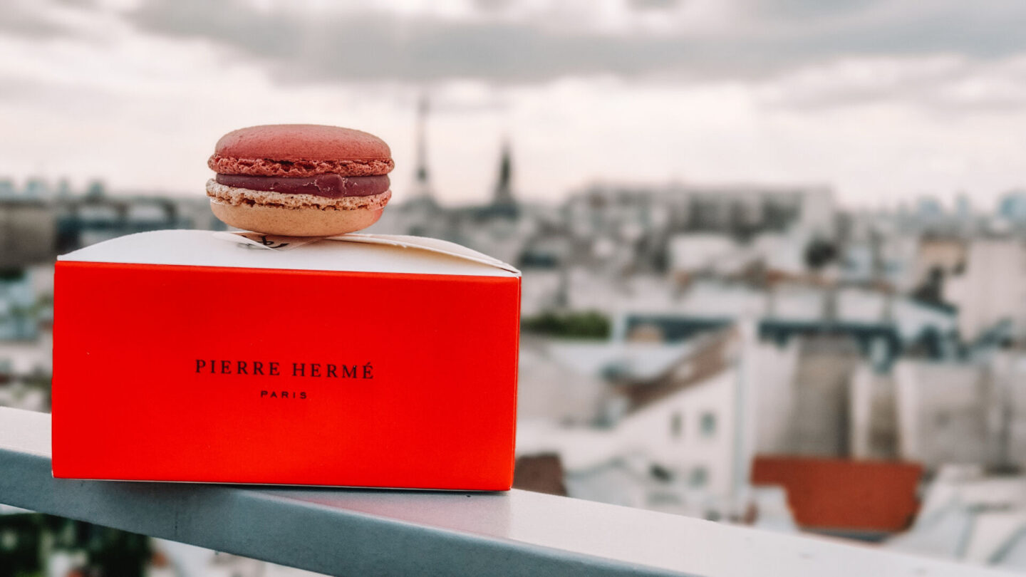 Pierre Hermé Ispahan macaron with red Pierre Hermé box overlooking Paris